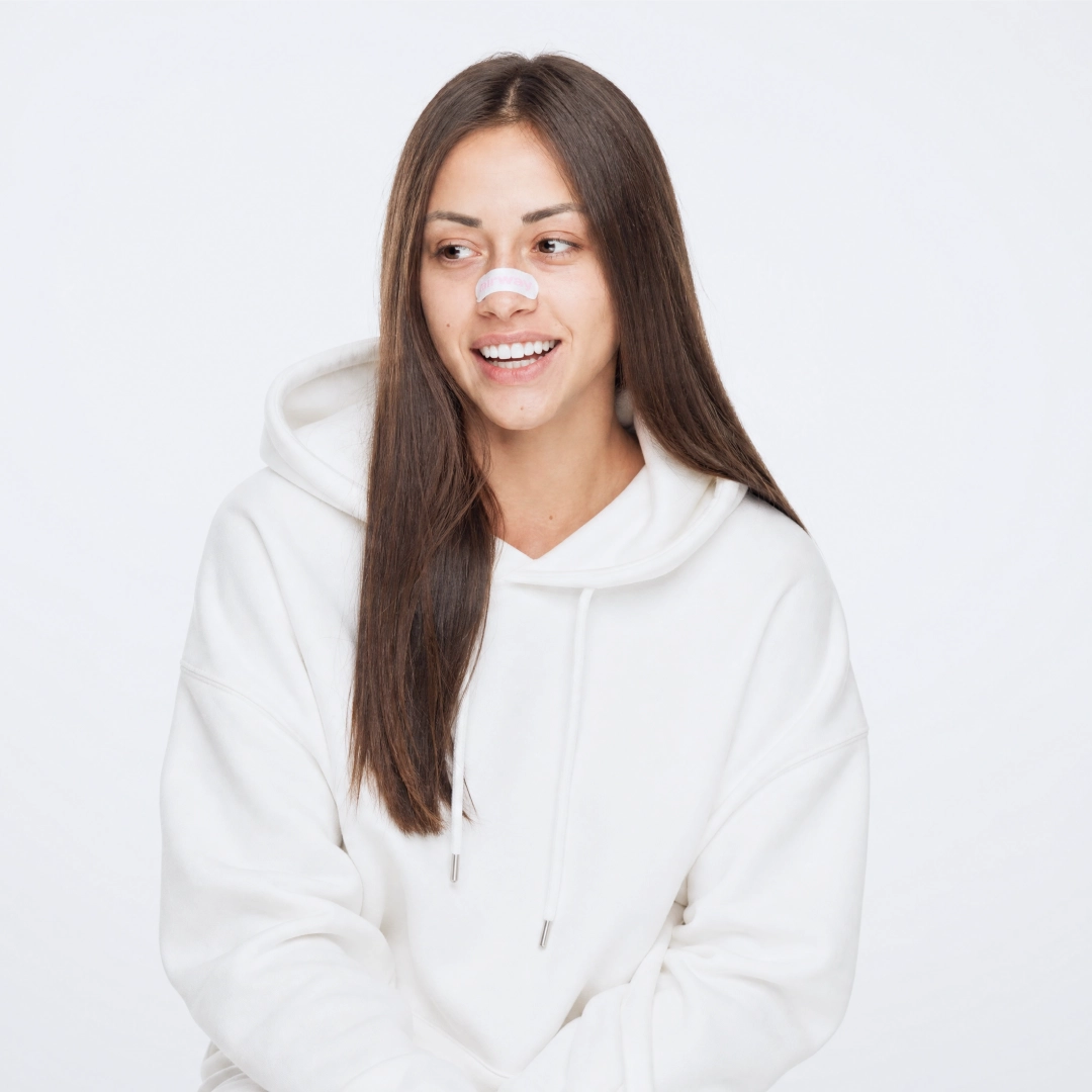 A woman with long brown hair wearing a white hoodie and a white and pink Airway nasalstrip.
